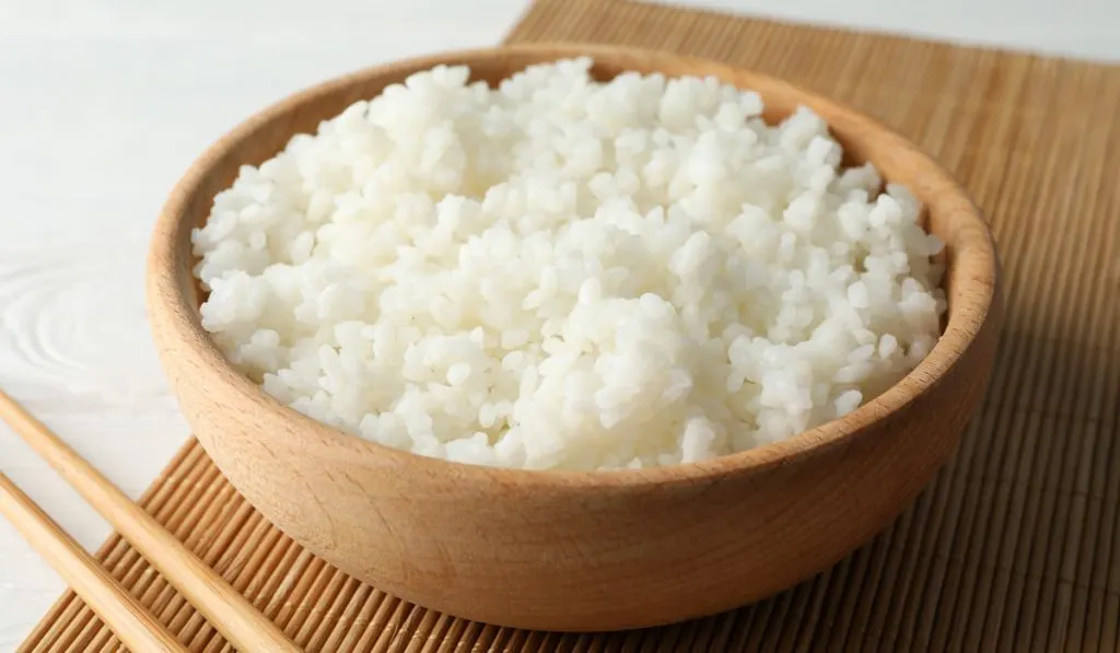 Bowl with boiled rice and chopsticks on wooden background