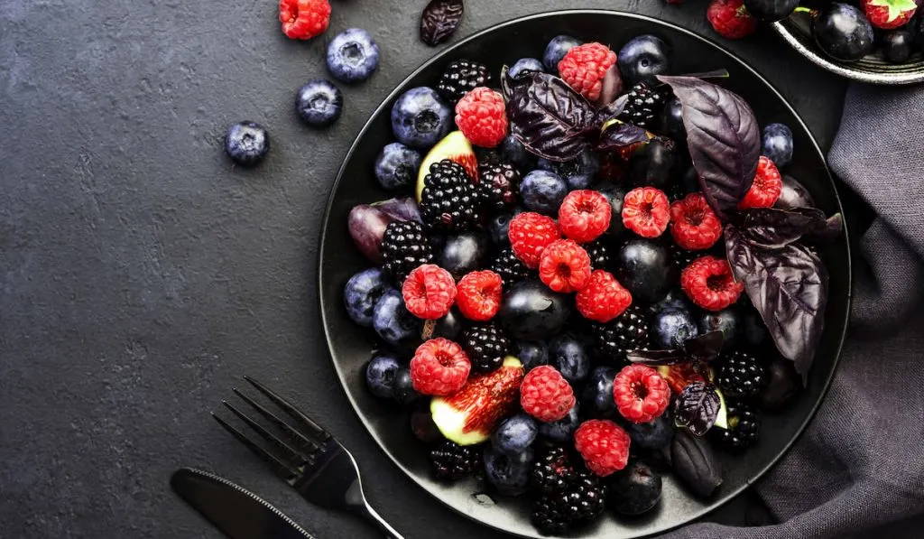 different types of berries on black plate black background