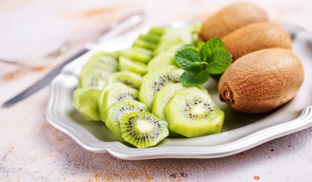 whole and slices of fresh kiwi on white plate